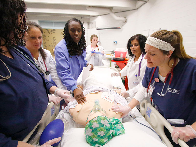 CCAC Nursing students gather around a training mannequin for hands-on learning experiences.