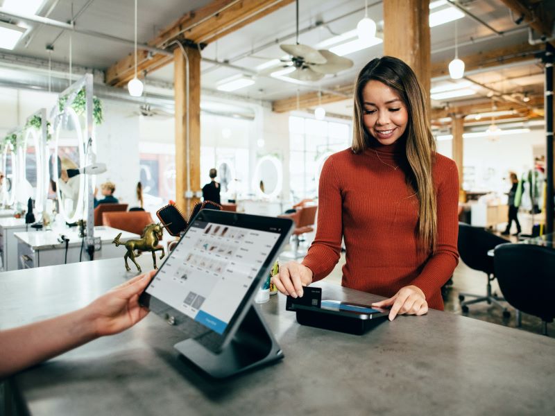 A woman scans her credit card at a boutique's checkout counter.