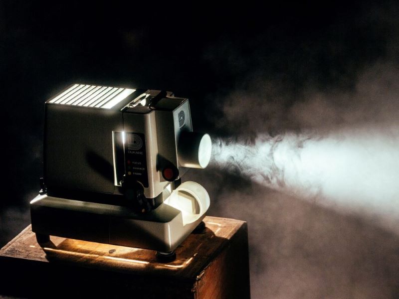 The bright light of a film projector cuts through the haze of a smoke-filled room. 