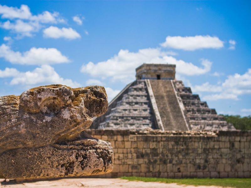 Ancient stone sculptures frame a Maya temple at Chichen Itza in Mexico.