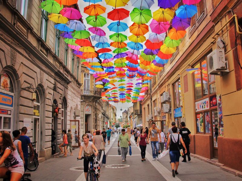 An installation of colorful umbrellas frames an unknown city street filled with pedestrians.