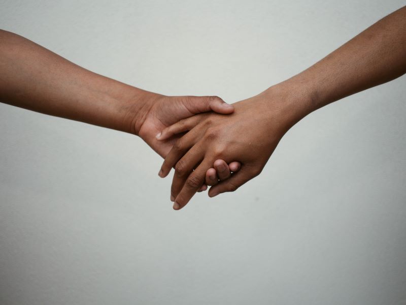Two people’s arms reach across empty space to hold hands affectionately.