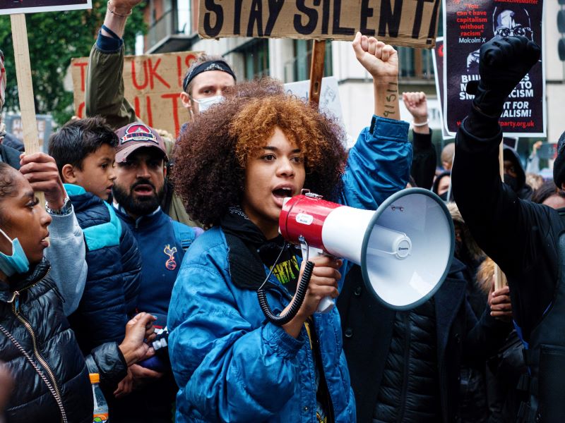 A woman with a bullhorn leads a crowd of protestors as they march down a street.