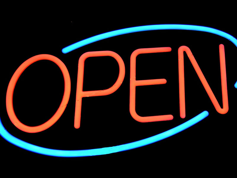 A neon open-for-business sign with a blue oval and red letters.