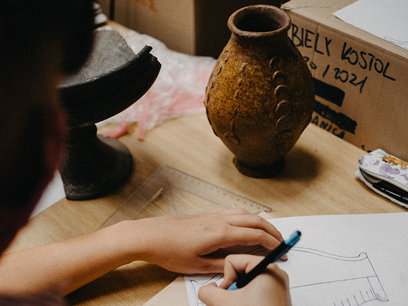 An archaeologist carefully sketches a rust-colored ceramic vase unearthed during a dig.