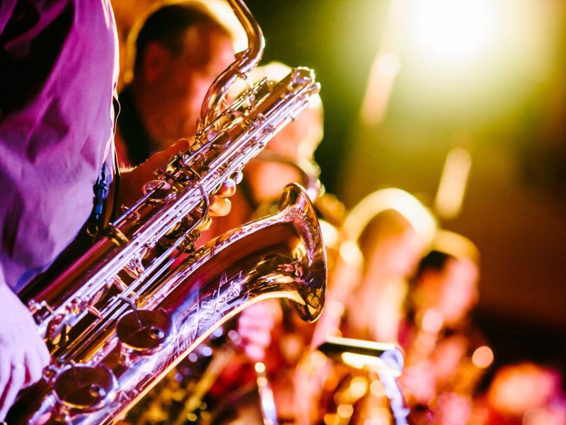 A row of saxophonists glow under stage lights during a performance.